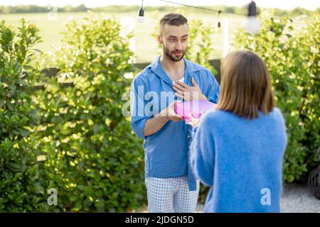 L'uomo dà un regalo in scatola rosa alla sua donna, celebrando all'aperto Foto Stock