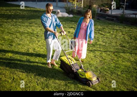 La giovane famiglia si prende cura del prato la sera d'estate Foto Stock