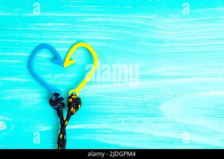 Simbolo del cuore realizzato con due bracciali a gancio di pesce a corda intrecciata disposti su sfondo di legno blu con spazio copia. Foto Stock
