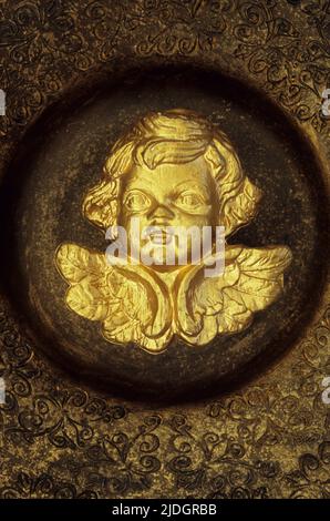 Testa e ali di cherubino dipinte d'oro giacente al centro di oro ornately modellato e ceramica marrone Foto Stock