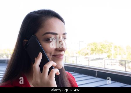 Parlando con il telefono, eccitata giovane donna d'affari che parla con il telefono. Nel balcone dell'ufficio, fare una pausa per parlare con amici, genitori, famiglia. Foto Stock