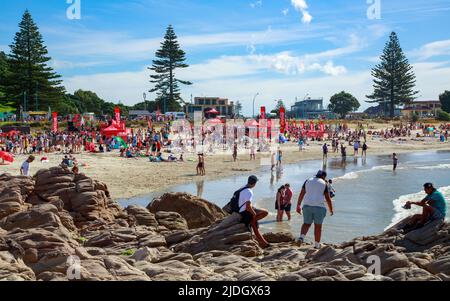 La spiaggia del Monte Maunganui, Nuova Zelanda, in una calda giornata estiva, affollata di persone e banner Coca-Cola da un evento sponsorizzato Foto Stock