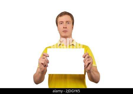 Serio ragazzo bello che tiene foglio di carta bianco, mockup di carta isolato su sfondo bianco. Uomo neutro in T-shirt gialla con carta mock up, unemotive e. Foto Stock