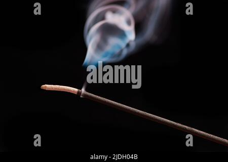 Ricci di fumo da incenso bruciante bastone per il relax e la meditazione, sfondo nero. Sessione di aromaterapia con bastone aromatico ardente con p turchese Foto Stock