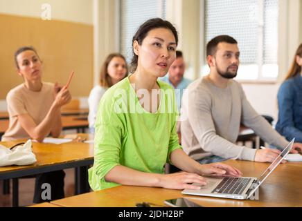 Donna intelligente che studia in classe, ascolta la conferenziera e scrive in notebook e notebook Foto Stock