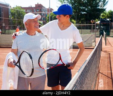 nonno e nipote parlano sul campo giocando a tennis Foto Stock
