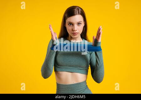 Ragazza sportiva con elastico per il fitness su sfondo giallo Foto Stock