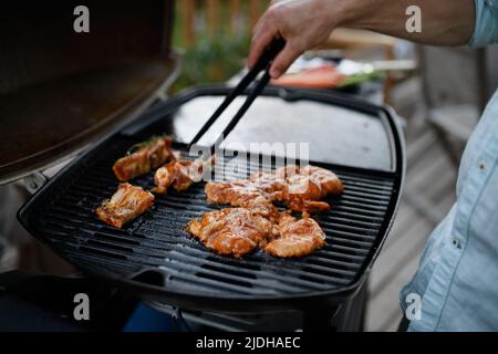 Carne, costolette e ali alla griglia irriconoscibili per l'uomo, alla griglia durante la festa estiva in famiglia, primo piano Foto Stock