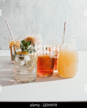 Varie bevande analcoliche rinfrescanti in bicchieri con ghiaccio. Succo di frutta diverso, limonata fatta in casa, caffè ghiacciato, tè alla frutta ghiacciata e frullati su una ba leggera Foto Stock