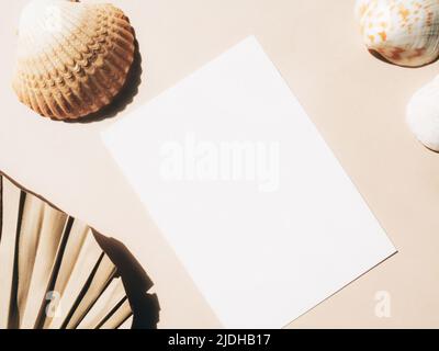 Carta bianca per mockup di testo, foglia di palma secca e conchiglia su sfondo beige. Concetto minimo per affari, messaggio o invito in pastello Foto Stock