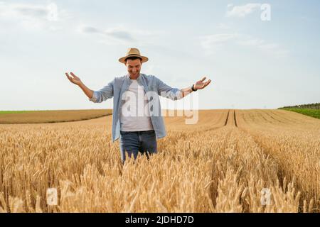 Un agricoltore felice è in piedi nel suo campo di grano in crescita. Foto Stock