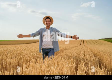 Coltivatore felice con le armi distese in piedi nel suo campo di grano crescente. Foto Stock