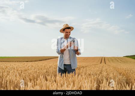 Agricoltore che usa il telefono cellulare mentre si trova nel suo campo di grano crescente. Foto Stock