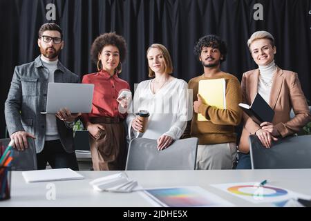 gruppo multietnico positivo di agenzia pubblicitaria che guarda la macchina fotografica in ufficio Foto Stock