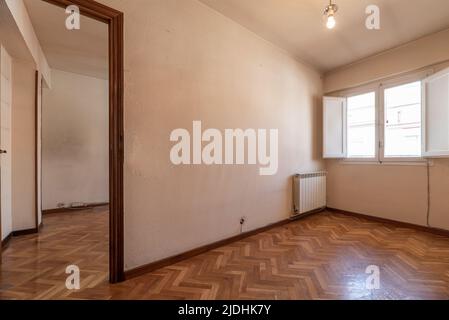 Camera vuota con pavimento in parquet di rovere luminoso, pareti dipinte di bianco e legno rossastro su porte e finestre in legno bianco con persiane Foto Stock