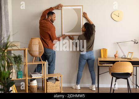 Black Millennial spose un Poster da appagare sul muro insieme a casa Foto Stock