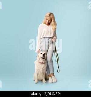 Concetto di amicizia. Donna felice in posa con il suo cane felice labrador su un guinzaglio, in piedi su sfondo blu Foto Stock