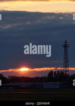 Una lacrima nelle nuvole pesanti consente al sole di intravedere un'ultima volta per silhouette una torre di controllo dell'aeroporto e sostenere gli edifici. Foto Stock