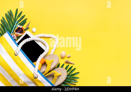 Accessori per il nuoto - borsa da spiaggia alla moda con strisce, occhiali neri, tavoletta bianca, foglia di palma, flop giallo su sfondo giallo Flat lay Top view Estate, viaggio, vacanza concept. Foto Stock