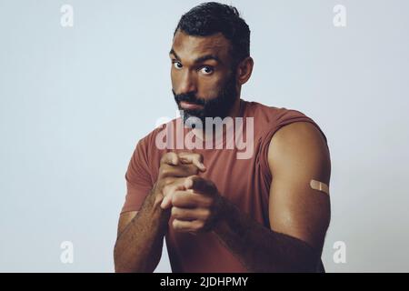 l'uomo vaccinato medio adulto bearded con il gesso sul braccio che punta alla macchina fotografica nel ritratto dello studio Foto Stock