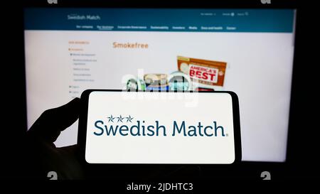 Persona che tiene lo smartphone con il logo della società di tabacco Swedish Match AB sullo schermo di fronte al sito web. Mettere a fuoco sul display del telefono. Foto Stock