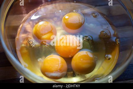 Primo piano uova, tuorli e albumi in una ciotola di vetro su un asse di bambù. Preparazione delle uova strapazzate. Foto Stock