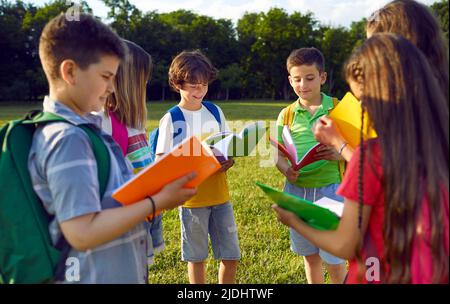 Gruppo di studenti delle scuole elementari leggono libri insieme in cerchio nel parco vicino alla scuola. Foto Stock