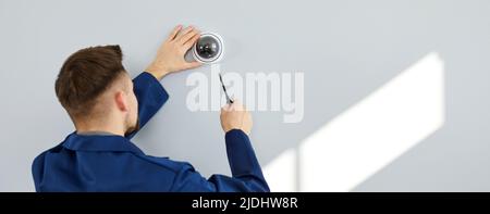 Lavoratore che installa la telecamera dome TVCC di sorveglianza moderna sulla parete all'interno dell'edificio Foto Stock