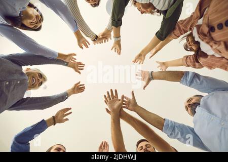 Vista dal basso del team di persone aziendali che si trovano in piedi insieme e che si uniscono alle loro mani Foto Stock