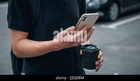 Primo piano, smartphone e un bicchiere di caffè nelle mani di un uomo. Foto Stock