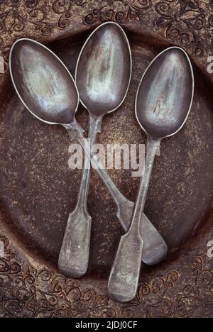 Tre antichi cucchiaini d'argento tarnished giacenti in una ciotola marrone e oro con motivo ornato Foto Stock