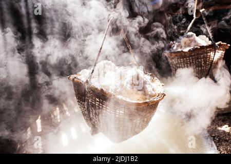 Sale di roccia bollente su forno a legna. Il sale è ancora prodotto nel modo tradizionale a Bo Kluea, Thailandia. Mettere a fuoco sul cestino di bambù del sale di roccia. Foto Stock