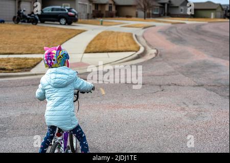 Ragazza che guida una bicicletta in modo sicuro attraverso la strada fino a un marciapiede indossando un casco. Foto Stock