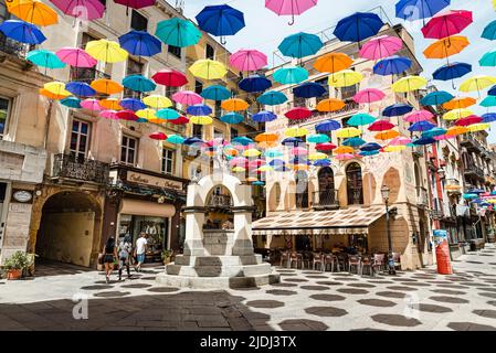 Gli ombrelloni colorati proteggono i passanti in Piazza Lamarmora, circondata da case storiche nel centro storico di Iglesias, nel sud-ovest della Sardegna, Italia Foto Stock