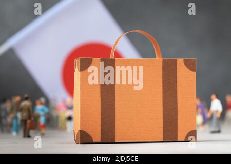 Valigia di cartone, giocattolo di plastica e una bandiera su sfondo astratto, un concetto sul tema del trasferimento o dell'immigrazione in Giappone Foto Stock