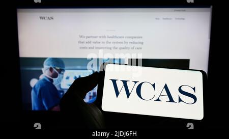 Persona che detiene il cellulare con il logo della società statunitense Welsh, Carson, Anderson e Stowe (WCAS) sullo schermo di fronte al sito web. Mettere a fuoco sul display del telefono. Foto Stock