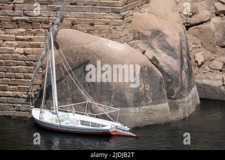 Felucca ormeggiata ad Assuan di fronte ai massi di granito con iscrizioni faraoniche, Egitto Foto Stock