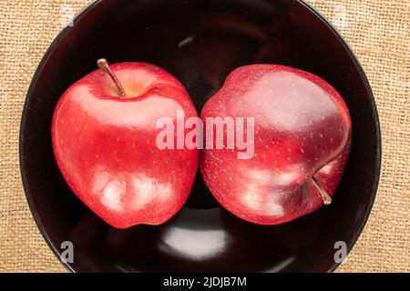 Due mele rosse mature in un piatto di ceramica su tela, primo piano, vista dall'alto. Foto Stock