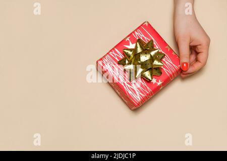 Una mano della donna raggiunge per una scatola regalo rossa con un arco giallo, un posto per il testo per copiare spazio Foto Stock