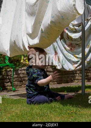 Toddler che gioca sotto la linea di lavaggio nel giardino, Regno Unito Foto Stock