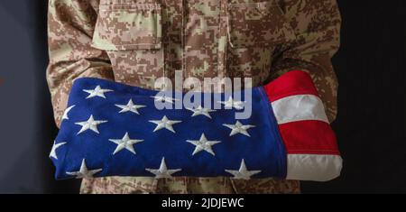 Militare americano soldato in USA militare modello digitale uniforme, tiene la bandiera fold. Stati Uniti, 4th luglio, giorno dell'indipendenza, uniforme camo, libertà degli Stati Uniti. Foto Stock