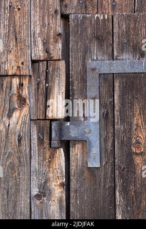 primo piano di una cerniera della porta arrugginita su una vecchia porta esterna. Accesso ad un fienile in legno intemperiato Foto Stock