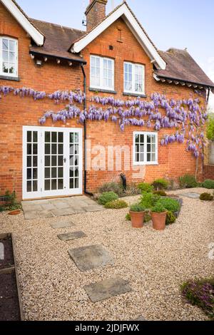 Casa vittoriana con finestre in legno, porte francesi e glicine. Giardino dal design paesaggistico con patio in pietra di York e pietre a gradini in ghiaia. ITA Foto Stock