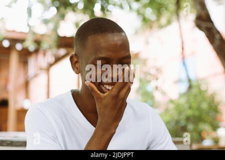 Sorridente, ridente e allegro uomo afroamericano che ricopre il viso a mano nella strada all'aperto. Nuovo lavoro, intervista Foto Stock