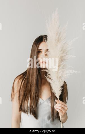 Ritratto di una bella ragazza con capelli lunghi con un bouquet di pampas erba sul suo viso. Ritratto di bellezza. Foto Stock