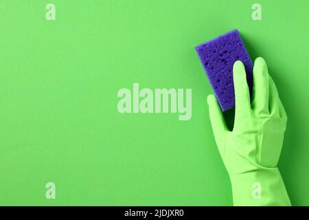 Mano femmina in guanto di protezione verde con spugna viola. Servizio di pulizia della casa e concetto di pulizia. Foto Stock