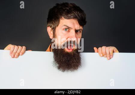 Confuso uomo barbuto con banner pubblicitari. Bel ragazzo mostra bordo vuoto con spazio per il testo Foto Stock