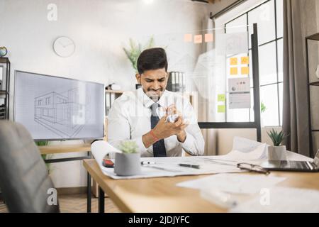 L'architetto arabo, uomo o costruttore maschile, ha sminuzzato un pezzo di carta con uno schizzo fallito, lavorare su un computer portatile sulla scrivania sul posto di lavoro in un ufficio moderno. Foto Stock
