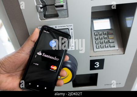 Uomo maschio adulto che tiene il telefono sulla sezione lettore di carte della biglietteria del treno con il nome della banca del fornitore della carta e il logo mastercard in mostra Foto Stock