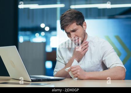 Sensazione di malessere sul posto di lavoro. Giovane bel uomo d'affari maschile, freelance che si ammala, mal di gola, tosse, influenza Foto Stock